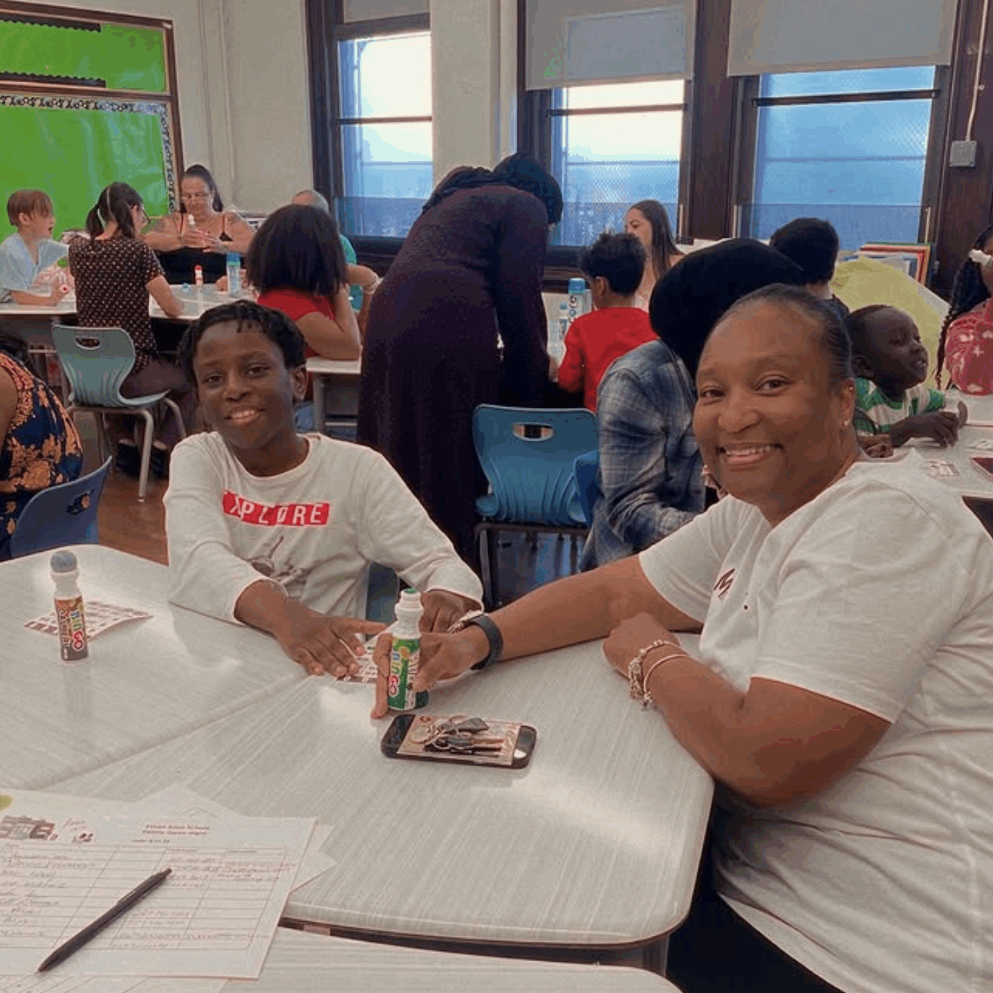 EthanAllen-Involved A smiling student and family member sitting together at a classroom table during a school community event, playing bingo with colorful markers.