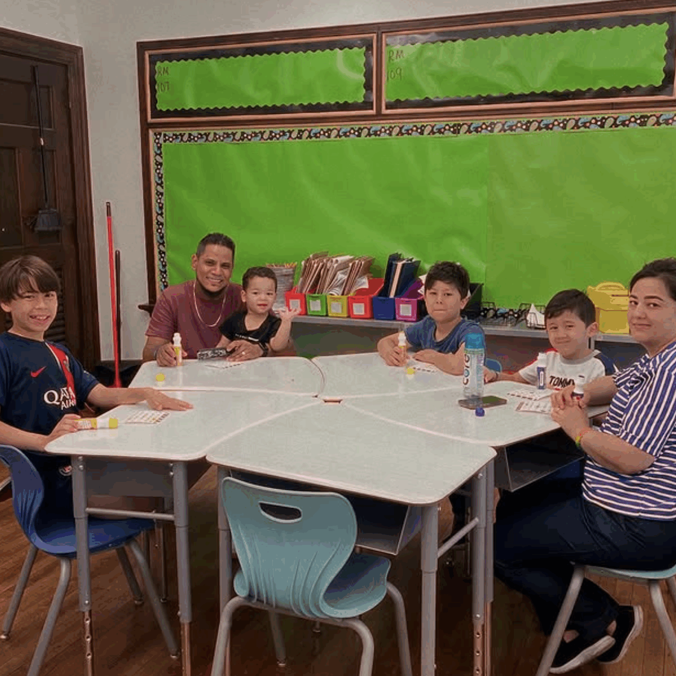 EthanAllen-Involved2 A family seated together around a classroom table at Ethan Allen School, participating in a school event with bingo cards and markers.